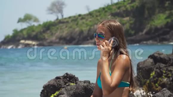 有手机的女孩坐在岩石上看着大海印度尼西亚巴厘视频的预览图