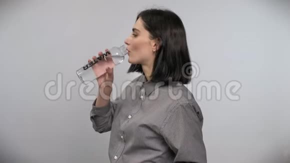年轻漂亮的女人棕色短发从瓶子里喝水白色背景视频的预览图
