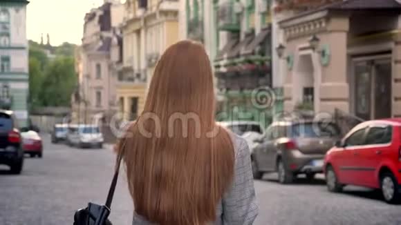 年轻女性留着长长的姜发一肩扛着背包在城市里散步城市街道背景视频的预览图