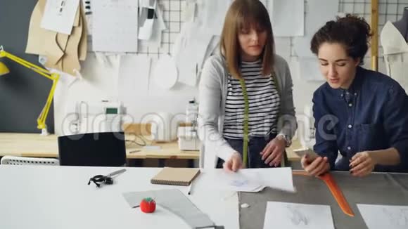 在设计行业工作的年轻女性在现代裁缝店工作时会比较素描和谈论素描视频的预览图