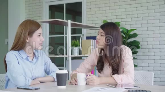两名年轻的亚洲女大学生或同事在办公室喝咖啡和交谈不同的群体视频的预览图
