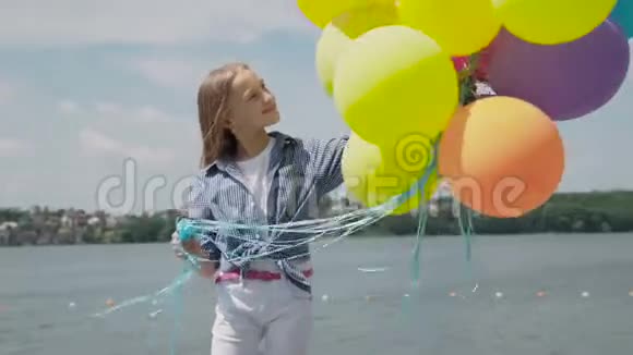 在池塘边放着五颜六色气球的小女孩的肖像视频的预览图