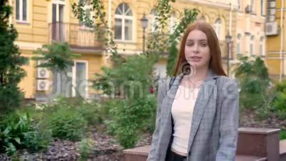 年轻自信的姜女穿着夹克走在城市的街上黄色的建筑背景视频的预览图