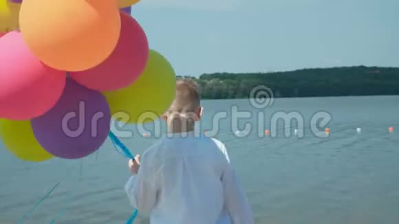 快乐的小男孩在湖岸上摆着五颜六色的气球4K视频的预览图