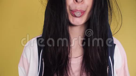 头发凌乱的漂亮女孩在黄色背景上吹口香糖视频的预览图