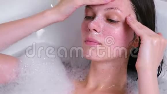 漂亮的黑发女人在浴室里的脸上涂了一层擦洗面的特写视频的预览图