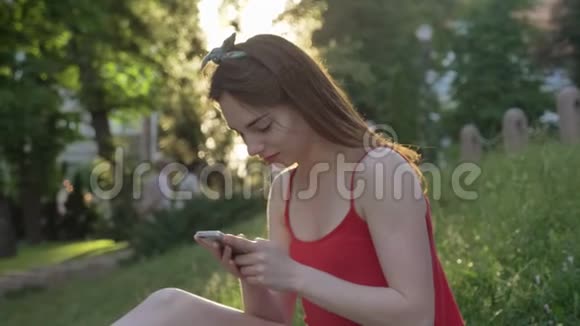 公园里一位金发碧眼的年轻美女坐在草地上打电话视频的预览图