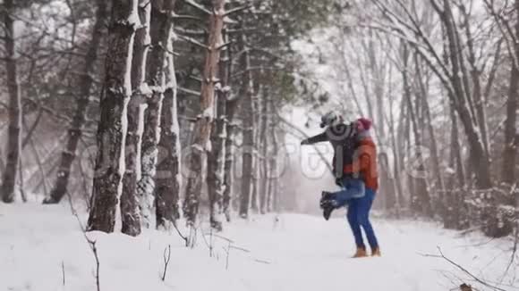 新郎旋转或转动快乐的新娘在下雪的天气松林中牵着她的手快乐视频的预览图