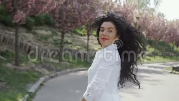 迷人的微笑的女人走在公园的小巷与盛开的树木视频的预览图