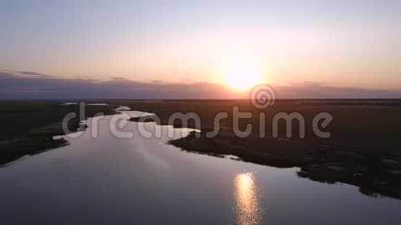 鸟瞰飞越美丽的河流在绿色的田野夕阳柔和的光和柔和的天空视频的预览图