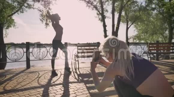 公园里的两个女朋友在拍照其中一个站着摆姿势拍照另一个则拿着电话公园视频的预览图