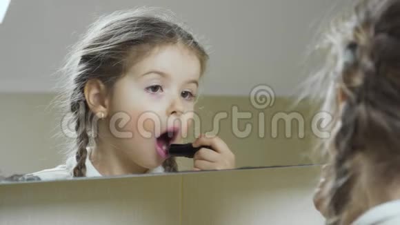 可爱的小女孩用口红在镜子的边缘涂上嘴唇视频的预览图