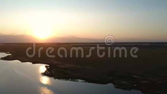 鸟瞰飞越美丽的河流在绿色的田野夕阳柔和的光和柔和的天空视频的预览图