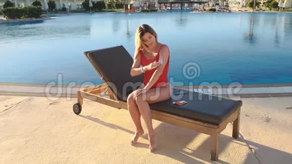 穿红色泳装的漂亮女孩在敏感皮肤上涂抹沐浴液以保护皮肤防止老化视频的预览图