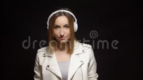 穿着白色耳机和黑色背景的白色皮夹克的可爱女孩视频的预览图