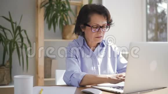 一位年长的女商人正拿着笔记本电脑坐在家里的办公室里视频的预览图