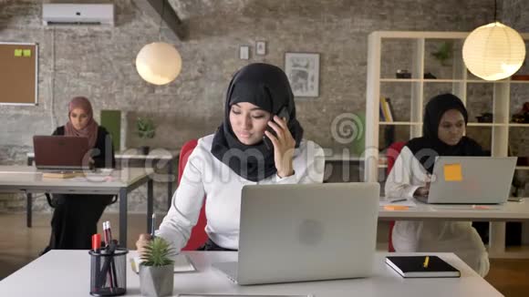 三位年轻的穆斯林妇女戴着头巾坐在现代办公室工作美丽的穆斯林妇女在电话中交谈视频的预览图