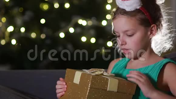 快乐的孩子打开圣诞礼盒卧室里戴着圣诞老人帽子的滑稽女孩孩子微笑的肖像视频的预览图