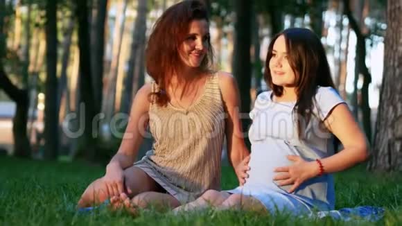 未来的妈妈和她的朋友坐在草地上视频的预览图