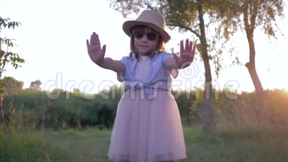 日落时分戴着墨镜和草帽的小女孩在镜头前跳舞视频的预览图