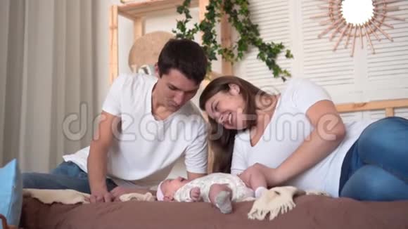 微笑的家庭在床上爸爸和妈妈正在看触摸和谈论他们的宝贝女儿视频的预览图