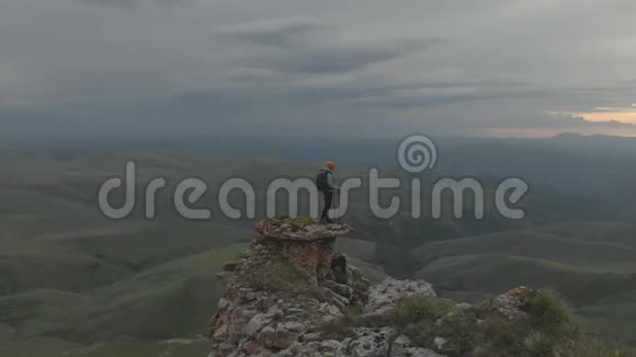 空中旅行在一个年轻的成年妇女周围走动她背着一个背包到达史诗般高原脚下的岩石顶部视频的预览图