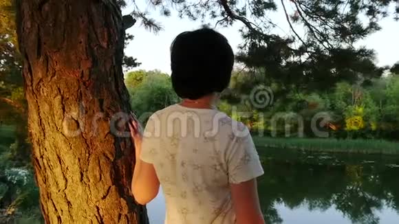 女孩站在河岸上看着水摄像机从后面缓慢移动松林视频的预览图