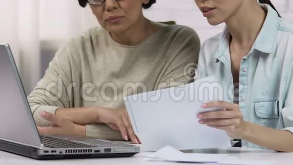 年轻女性在家里用笔记本电脑向母亲展示在线支付软件视频的预览图