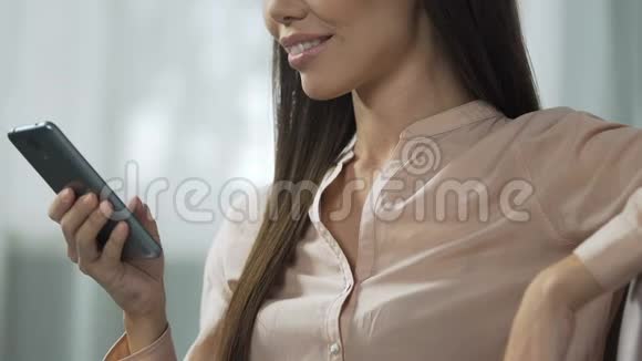 坐在客厅沙发上的美女在智能手机上滚动购物应用视频的预览图