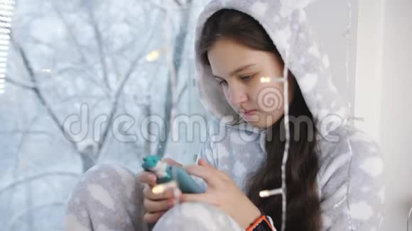 少女冬窗穿着暖和的睡衣带着智能手机视频的预览图