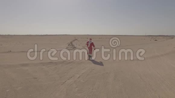 俄罗斯圣诞老人或德德莫罗兹带着麻袋走在沙子上在沙漠中找到了沥青路日志简介空中观景无人机视频的预览图