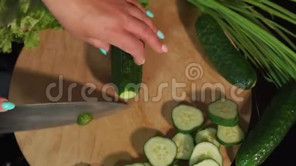 女人在黑色背景的木板上切鲜黄瓜的特写镜头视频的预览图