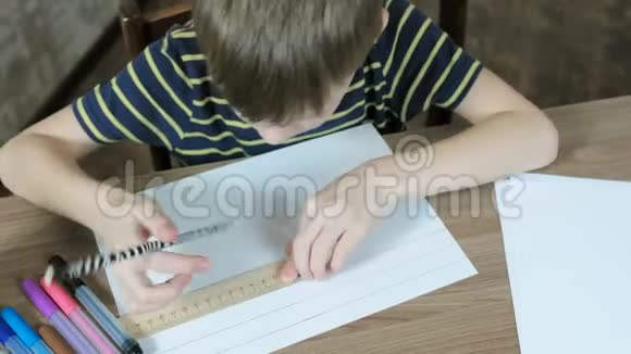 7岁的男孩穿着条纹t恤用铅笔和尺子在纸上画均匀的线条上景视频的预览图