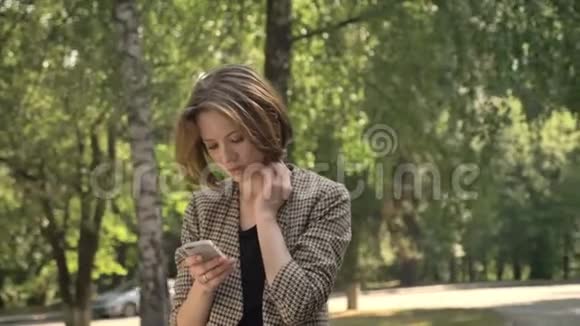 年轻有魅力的集中女孩白天在公园的智能手机上输入信息夏天在公园里输入信息视频的预览图