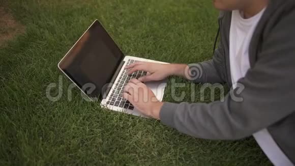 无法辨认的人躺在草坪上的笔记本电脑上打字侧视视频的预览图