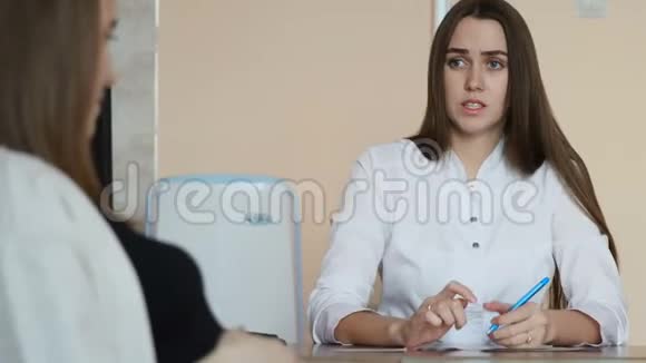 一位穿着黑色T恤的年轻漂亮孕妇正在和一位穿着白色外套的年轻女医生谈话视频的预览图