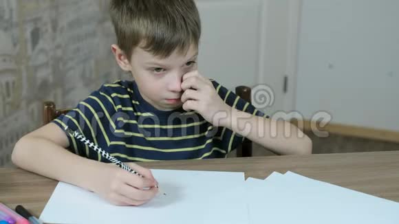 七岁的男孩穿着一件带条纹的t恤用一支简单的铅笔在桌子旁画椭圆形视频的预览图