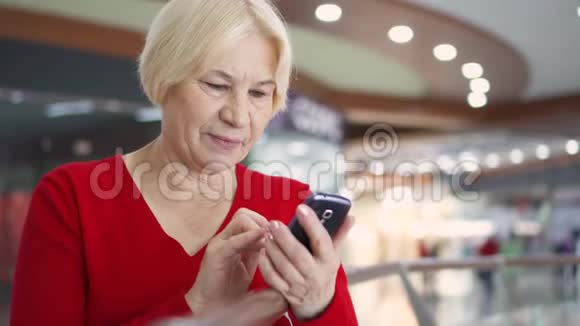 商场里的老太太微笑着使用她的智能手机浏览阅读新闻聊天视频的预览图