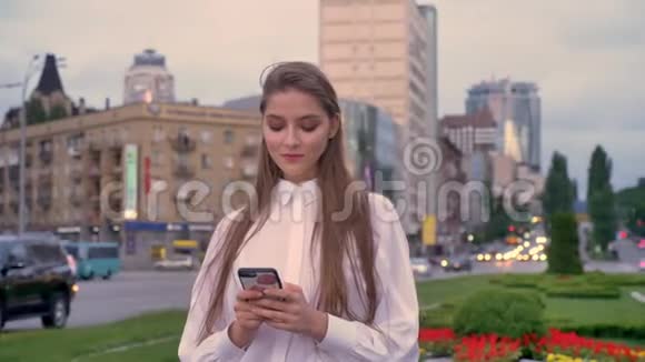 年轻快乐的女孩在夏天的日落时分在市中心的智能手机上输入信息思考概念交流视频的预览图