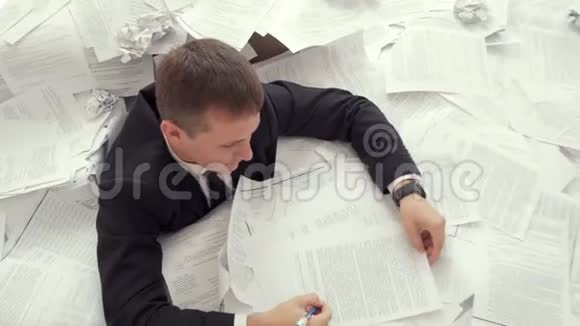 办公室员工无法应付文件数量一个疲惫的年轻人正坐在一堆文件里签名视频的预览图