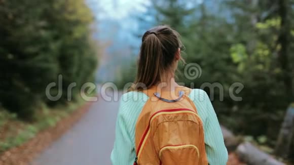 女徒步旅行者带着小背包走在森林里的路上视频的预览图