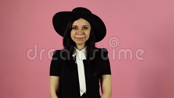 女士在粉红色的背景上微笑穿黑色连衣裙和帽子的女人视频的预览图