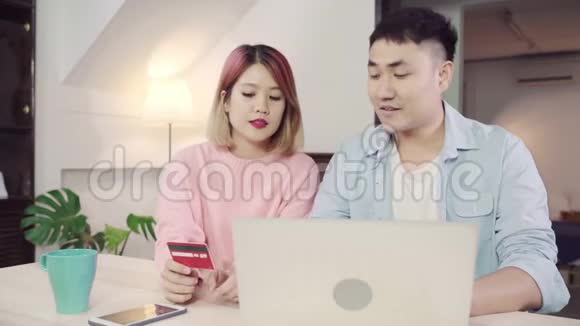 年轻的亚洲家庭夫妇使用笔记本电脑讨论新闻或做网上购物一起坐在办公桌上周末在家里视频的预览图