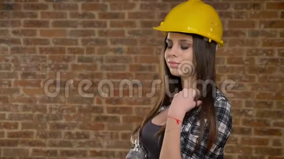 戴着头盔的年轻漂亮迷人的女人看着镜头捻着长发女建筑工人砖背景视频的预览图