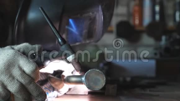 在车库或车间使用专业设备和防护面罩进行焊接工作的焊工关闭男子焊接视频的预览图