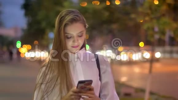 年轻迷人的恋爱女孩正在夏天的晚上在智能手机上输入信息微笑着交流理念视频的预览图