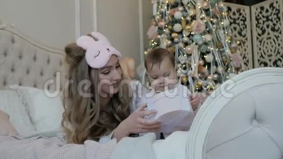 圣诞早晨妈妈和孩子的女儿在圣诞树的背景上带着礼物视频的预览图