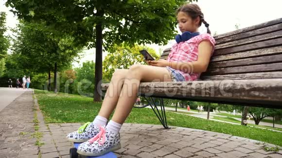 年轻女孩坐在公园的长凳上用智能手机打字视频的预览图