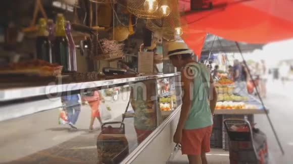 戴着草帽的少年看着水果蔬菜市场的熟食店橱窗视频的预览图