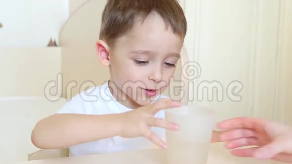 孩子坐在一张桌子旁从杯子里喝水然后微笑视频的预览图